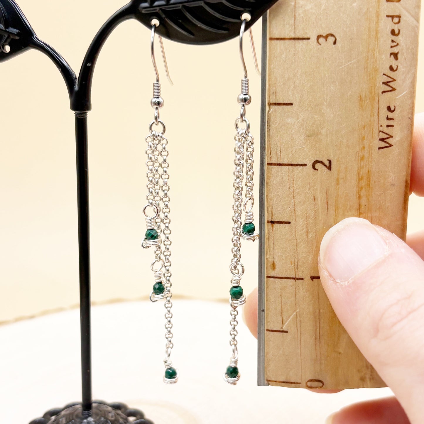 Silver chain earrings with green beads on a wooden ruler for scale.