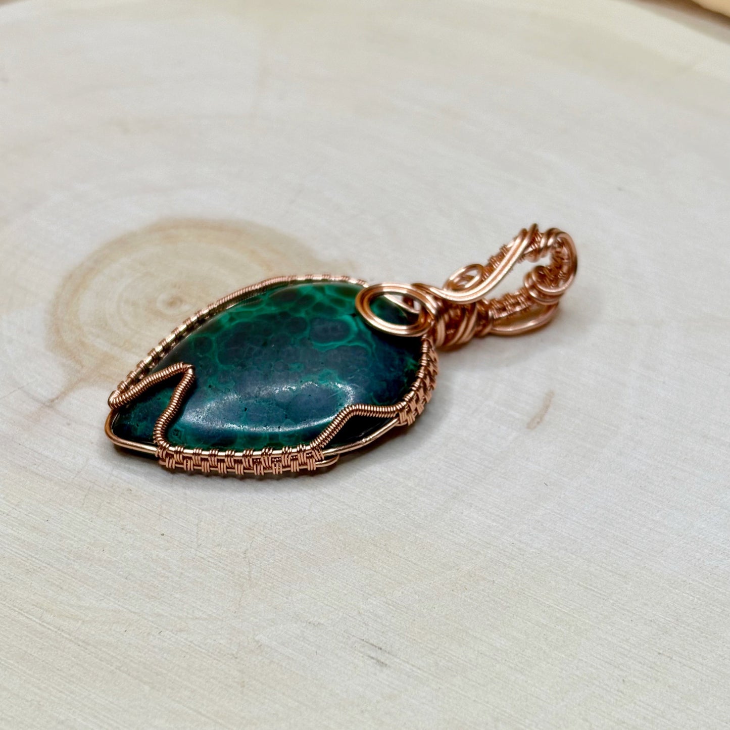 Green stone pendant with copper wire wrapping on a wooden surface
