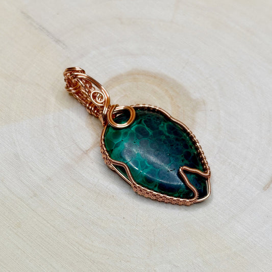 Green stone pendant with copper wire wrapping on a textured white surface
