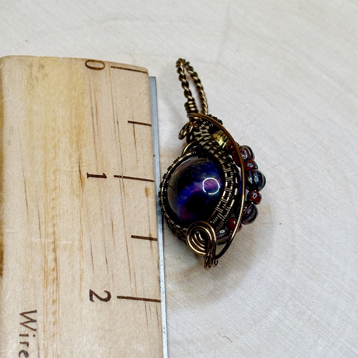 Jewelry pendant with a purple gemstone on a wooden block with measurement scale