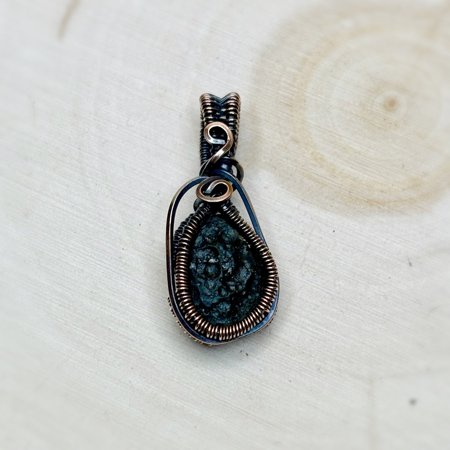 Moldavite tektite wire wrap jewelry sitting on a wooden background