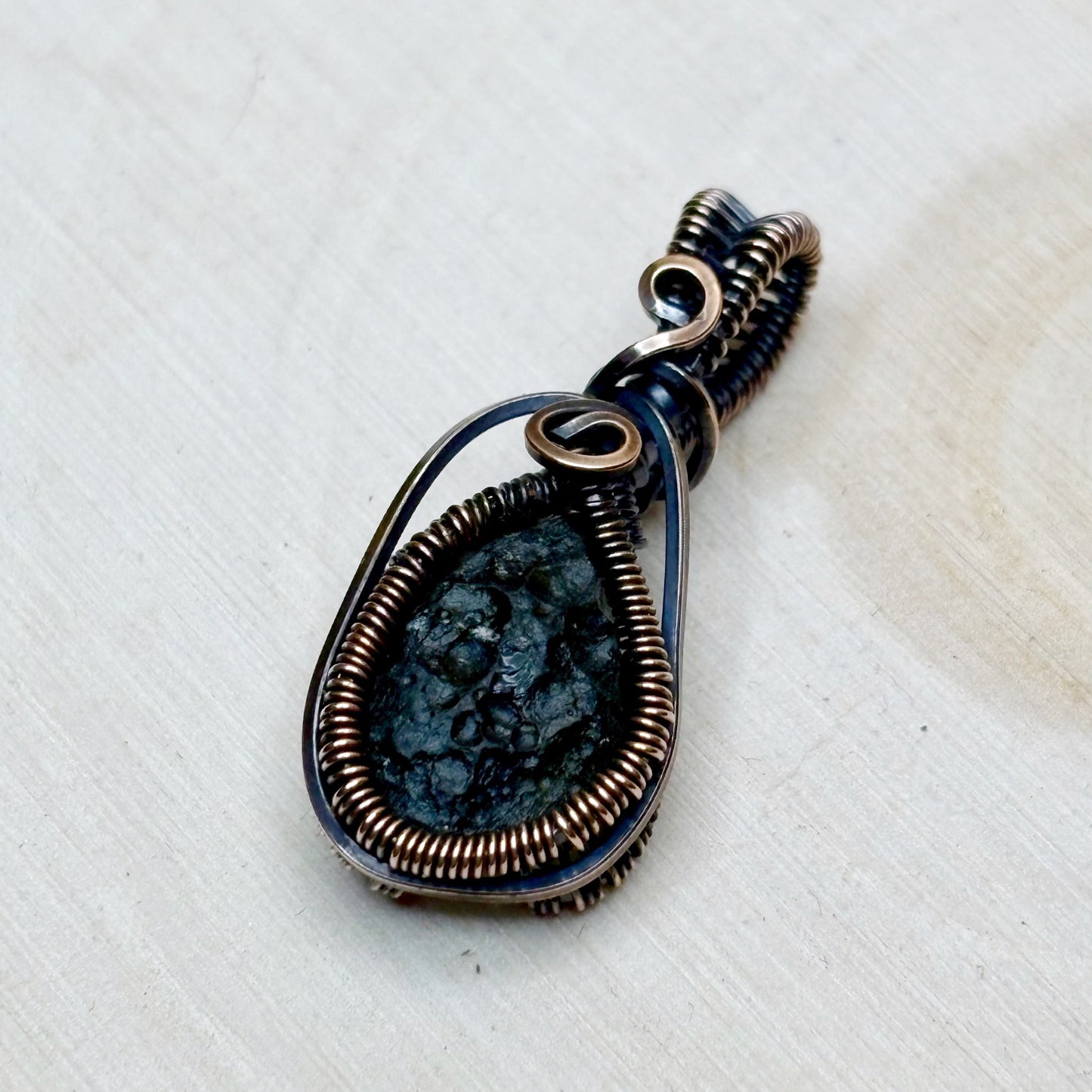 Pendant with green stone and copper wire wrapping on a textured white background