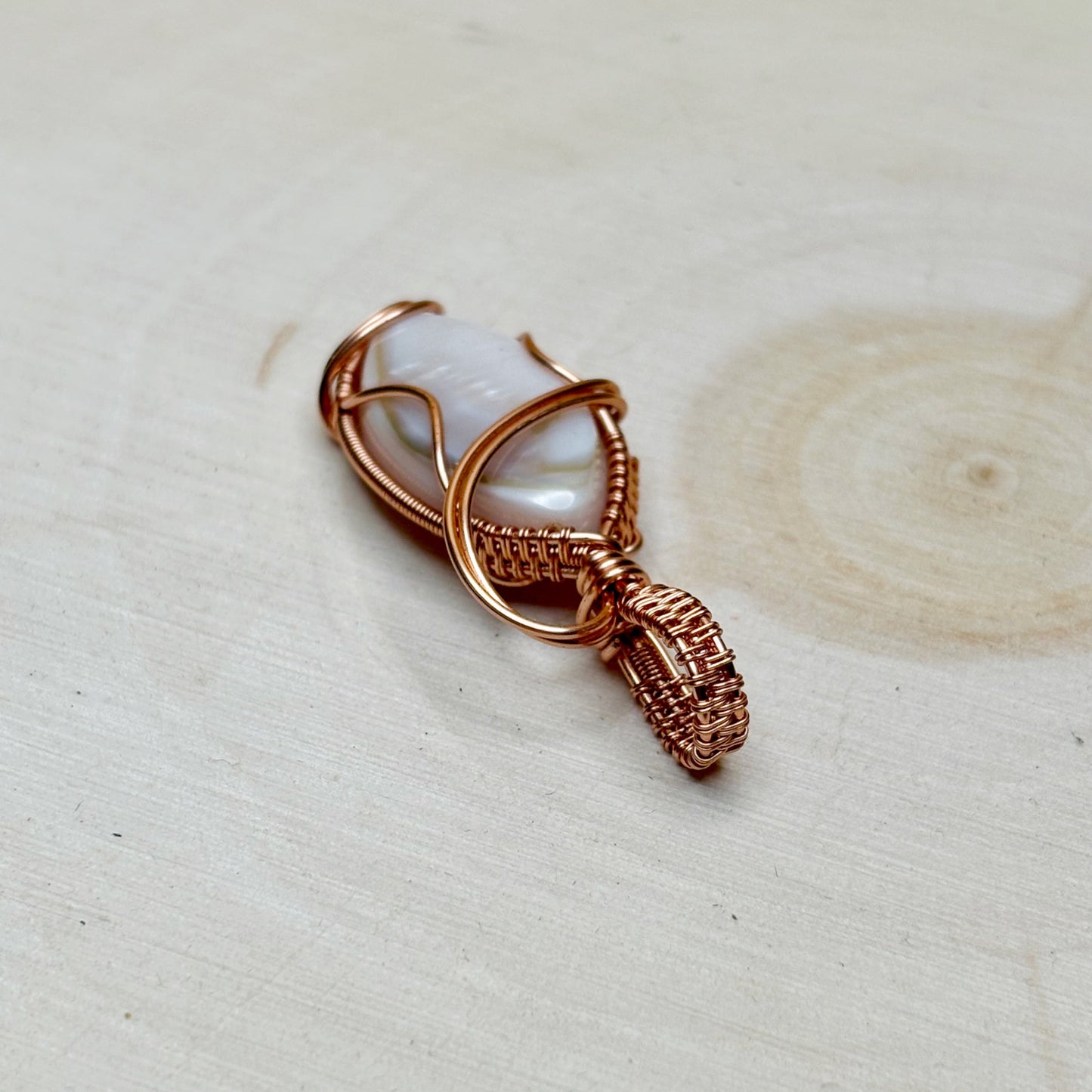 Copper wire wrapped mother of pearl shell sitting on a wooden light background