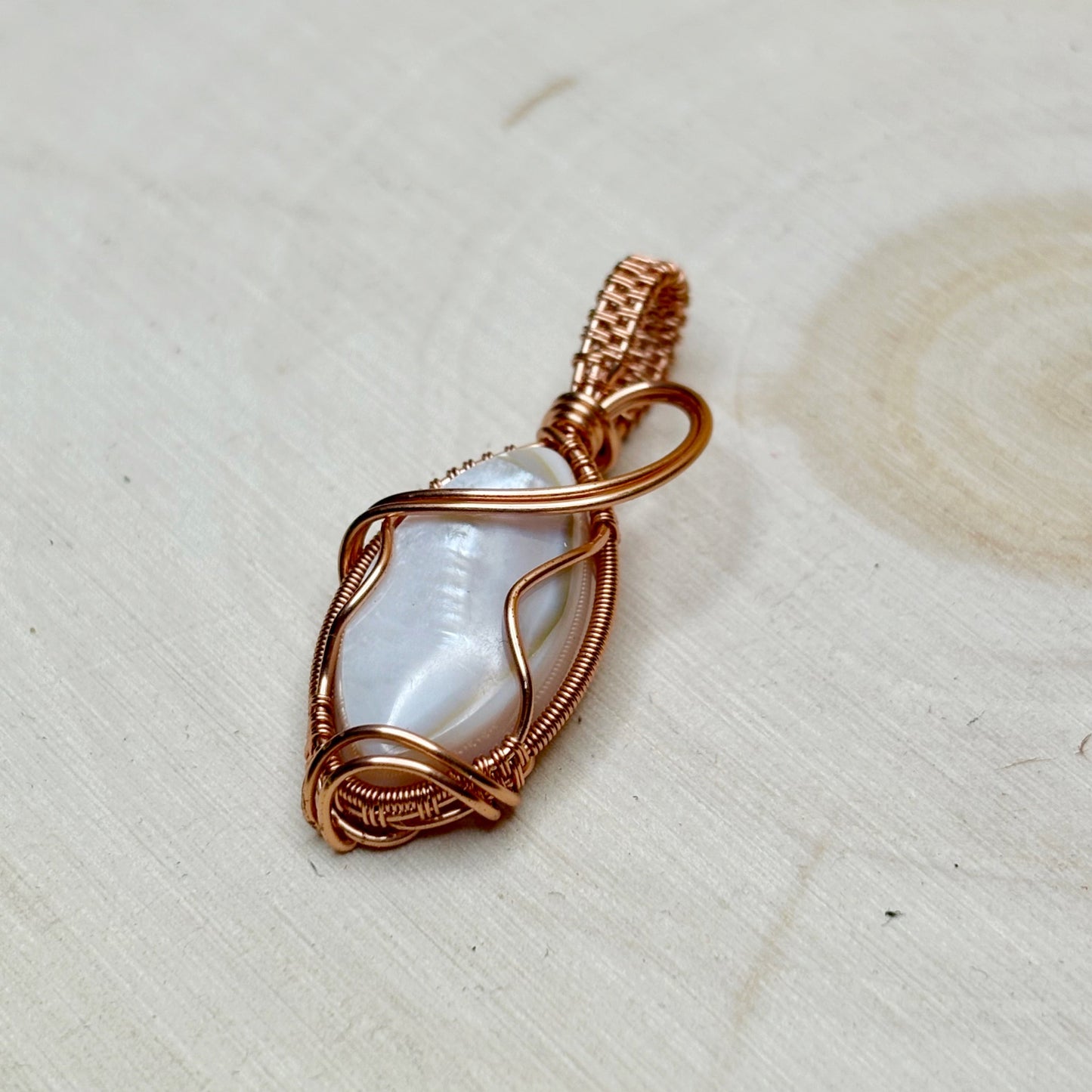 Copper-wrapped pendant with a central shell focal on a light wooden surface