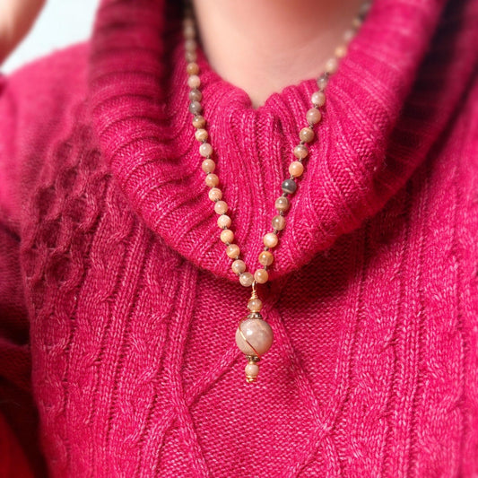 Person wearing a pink sweater with a beaded necklace