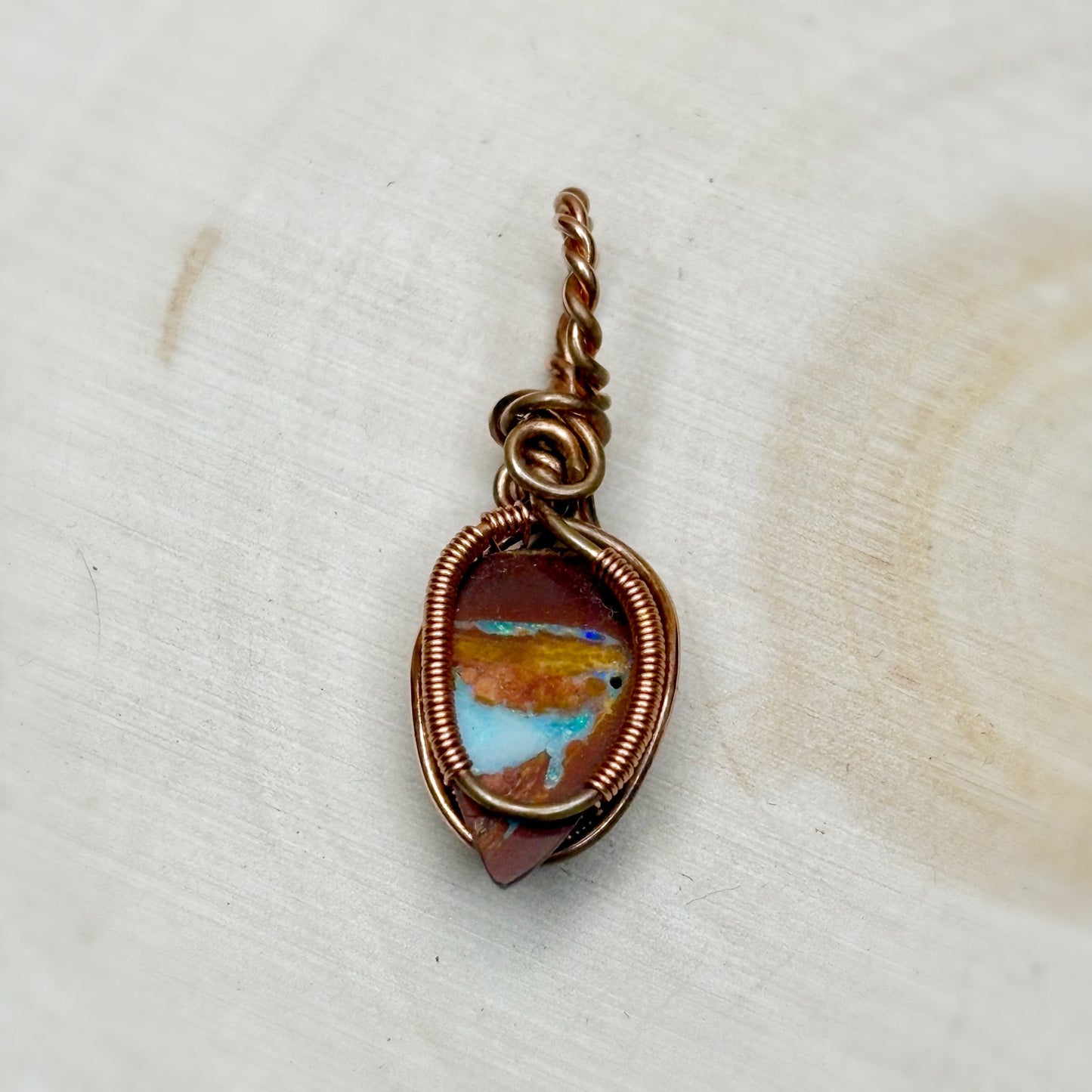 Jewelry pendant with a copper wire wrap and multicolored stone on a white background