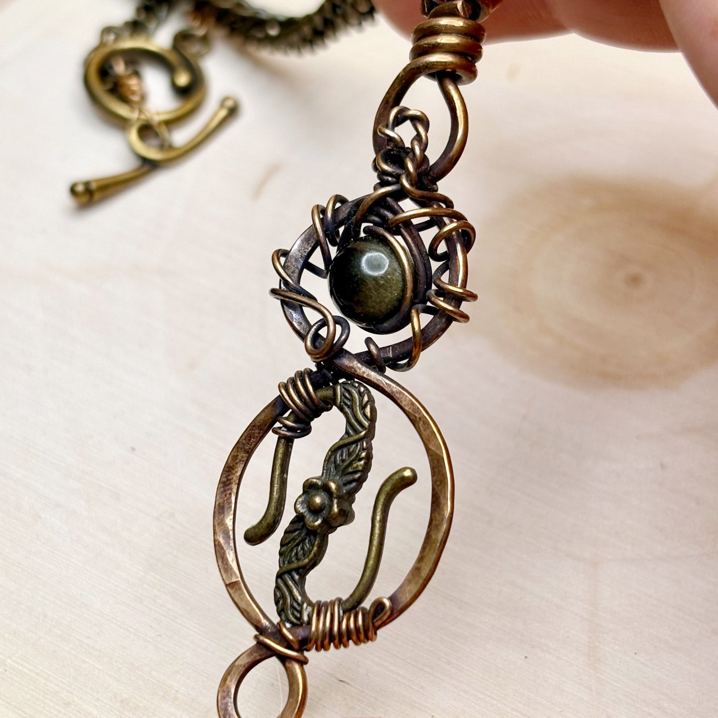 Close-up of a detailed bronze pendant with a central gold gemstone on a light background.