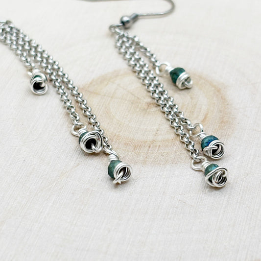 Silver chain earrings with green beads on a light wooden surface