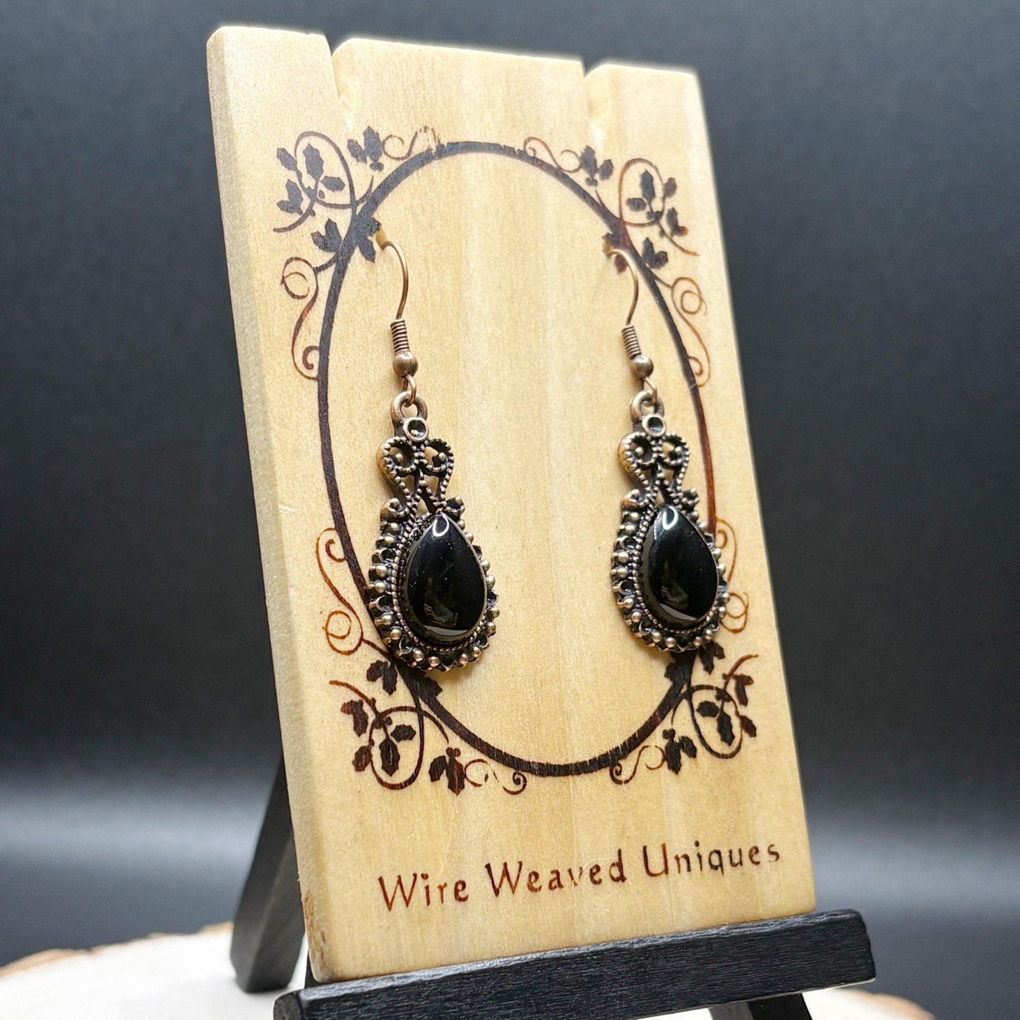 Pair of black teardrop earrings on a wooden display card with 'Wire Weaved Uniques' branding.