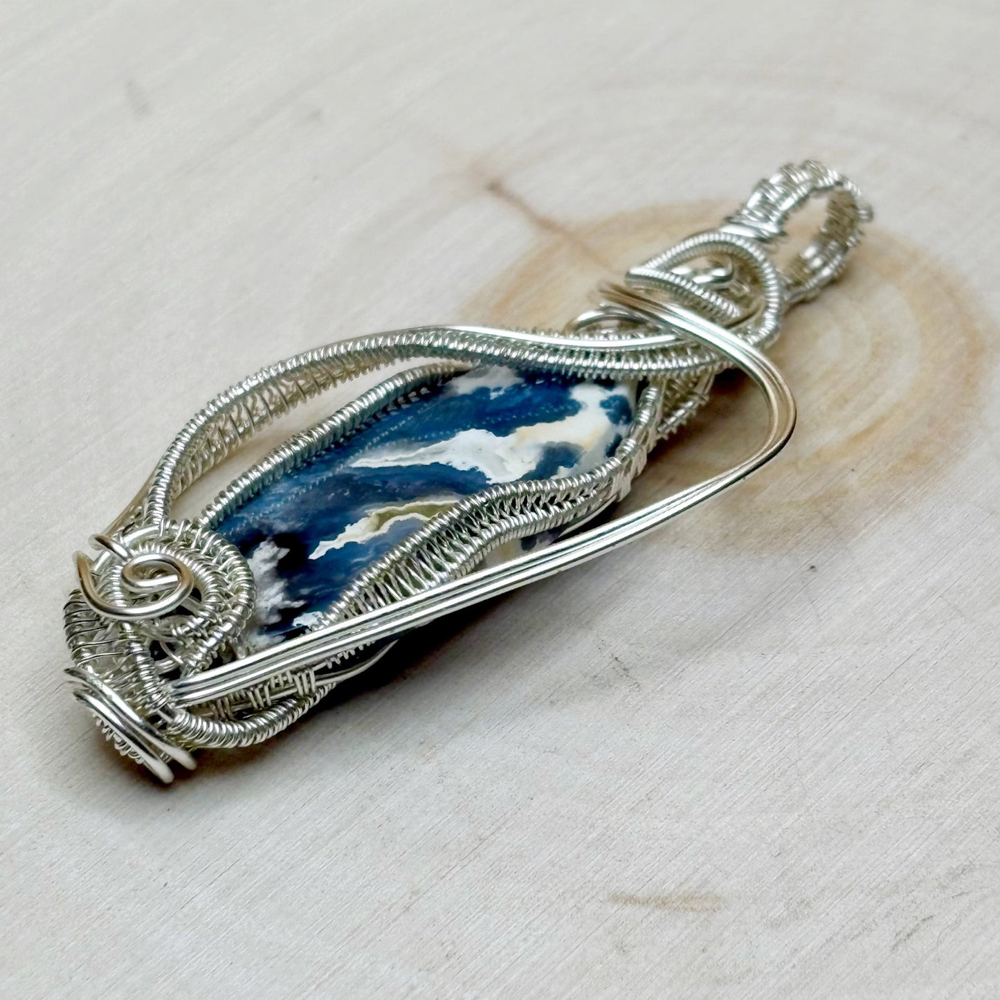 Silver wire-wrapped pendant with blue and white stone on a light background