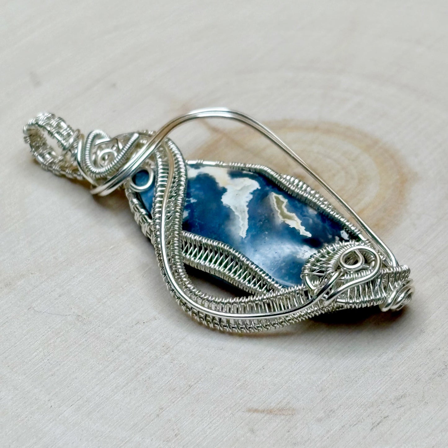 Silver pendant with blue stone on a beige background