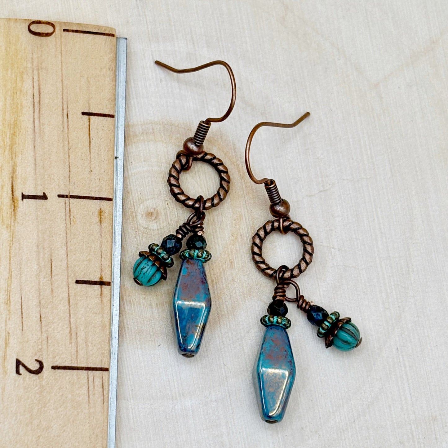 Pair of earrings with blue and green beads on a wooden ruler
