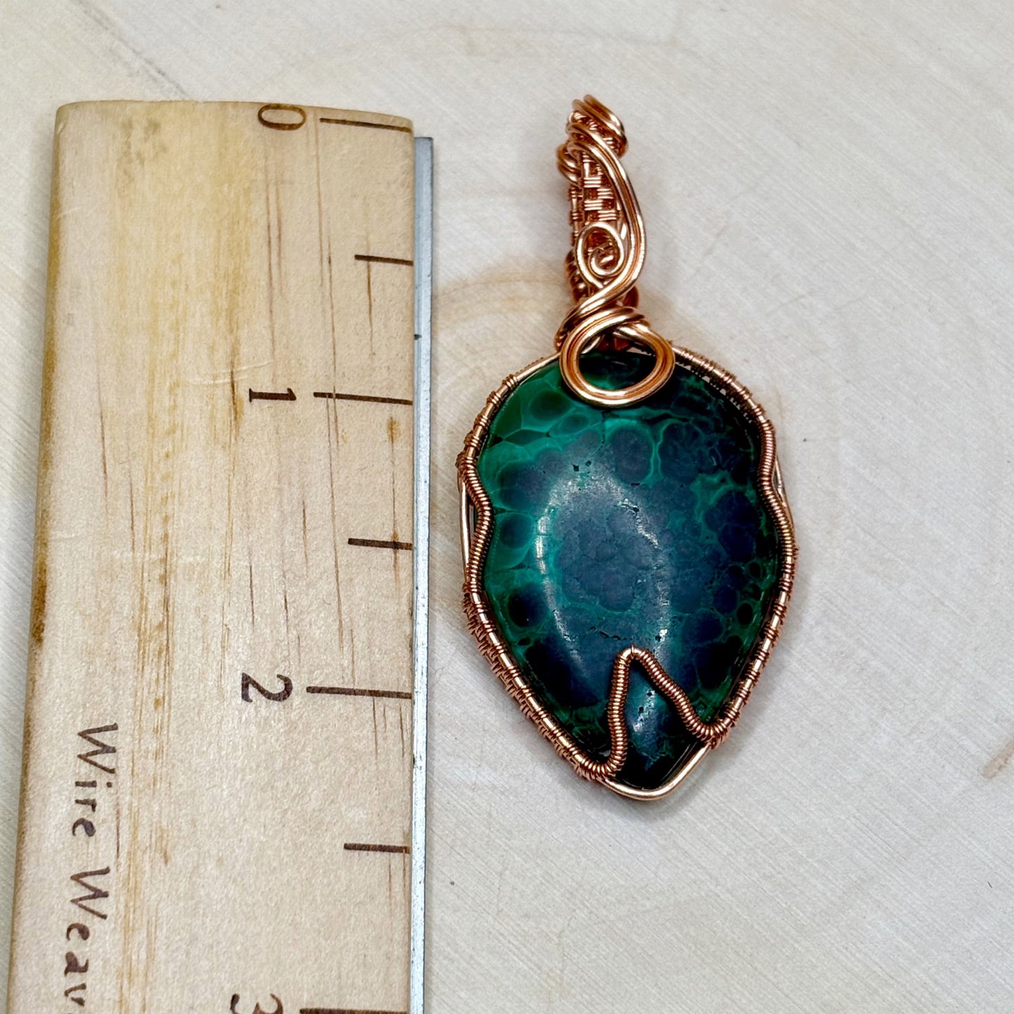 Green stone pendant with copper wire wrap on a wooden ruler