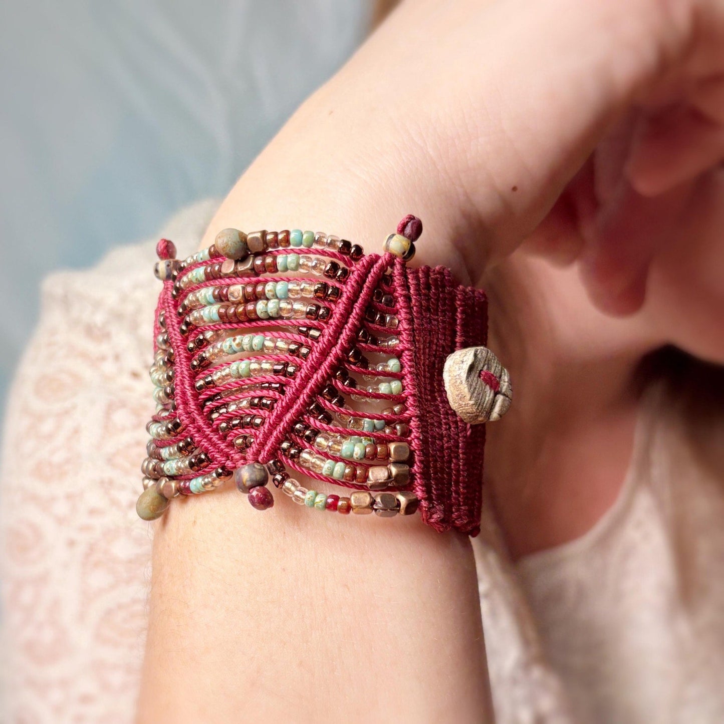 Close-up of a hand wearing a red beaded bracelet with a blurred background
