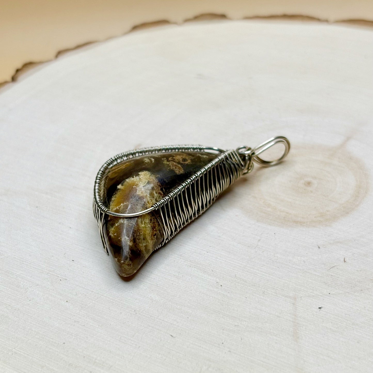 Crescent moon shaped amber wire wrapped in sterling silver necklace pendant sitting on a wooden background