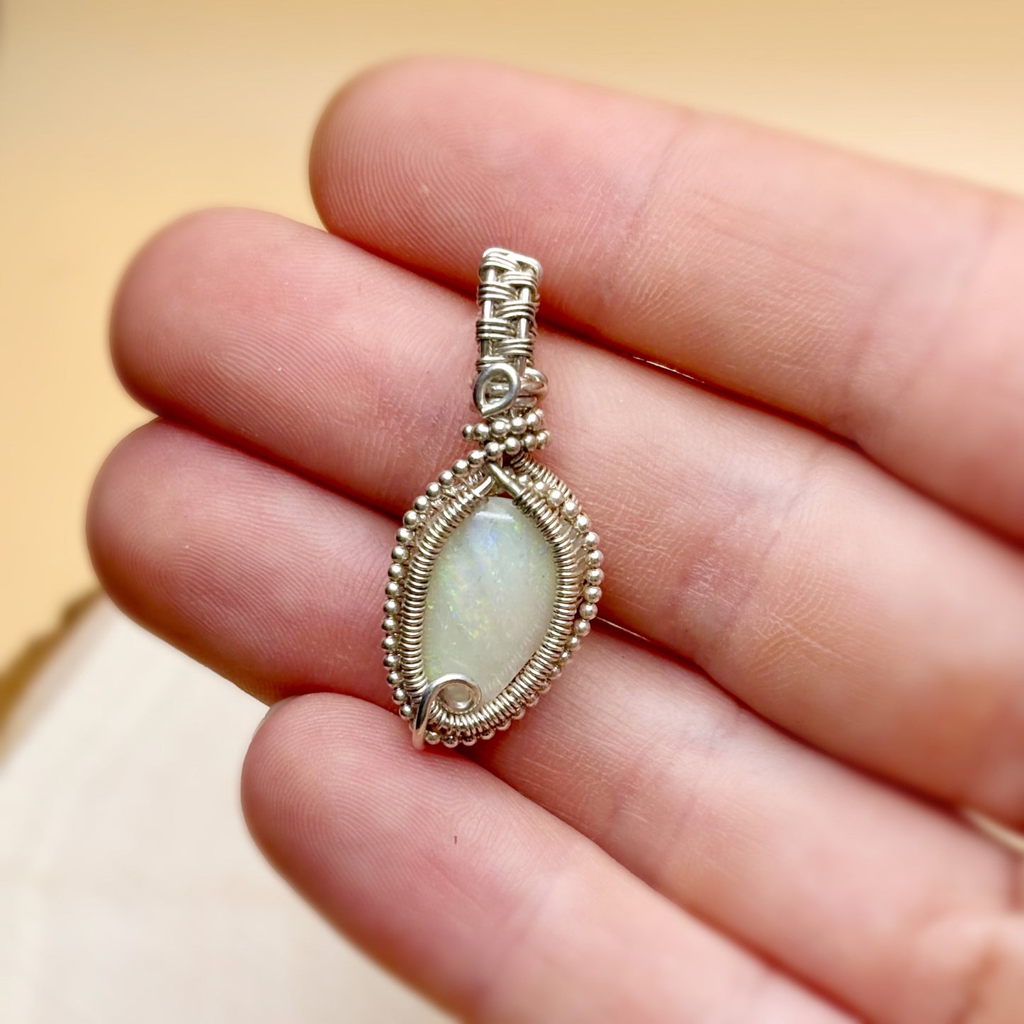 Silver pendant with a light stone held between fingers against a beige background