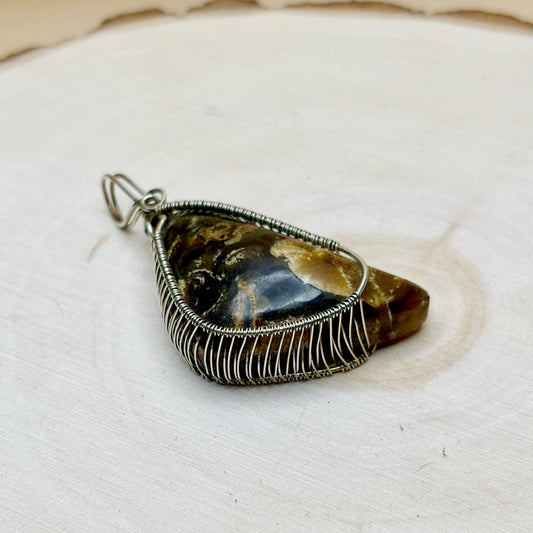 Wire-wrapped pendant with a natural amber stone in sterling silver on a light background