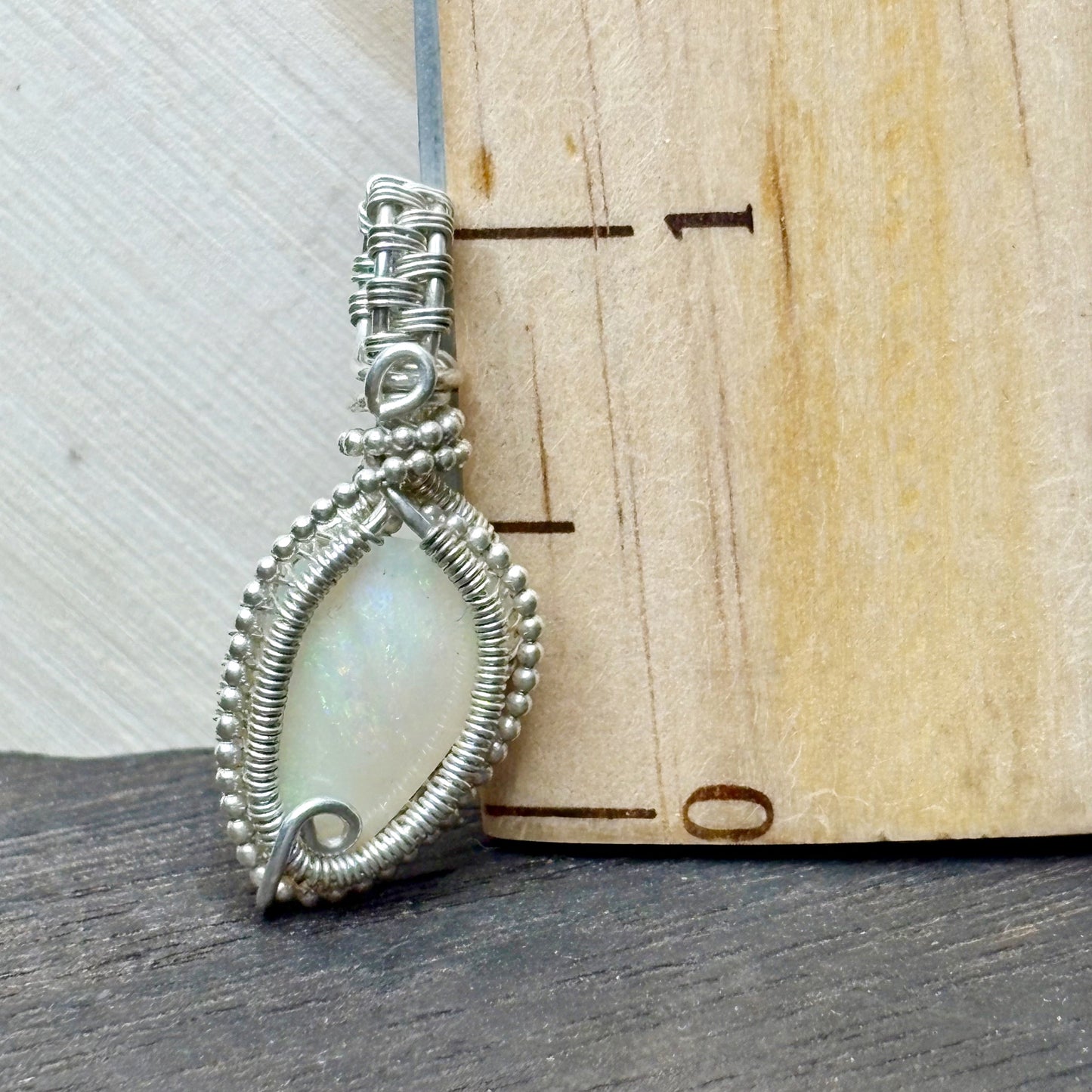 Silver wire-wrapped pendant with a light-colored stone on a wooden surface