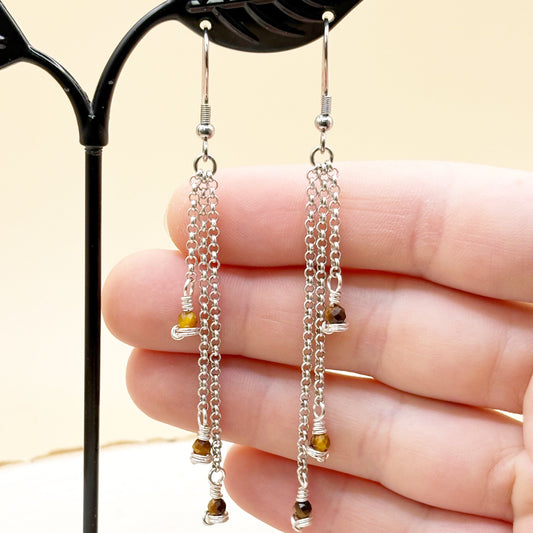 Silver chain earrings with small beads held between fingers against a neutral background