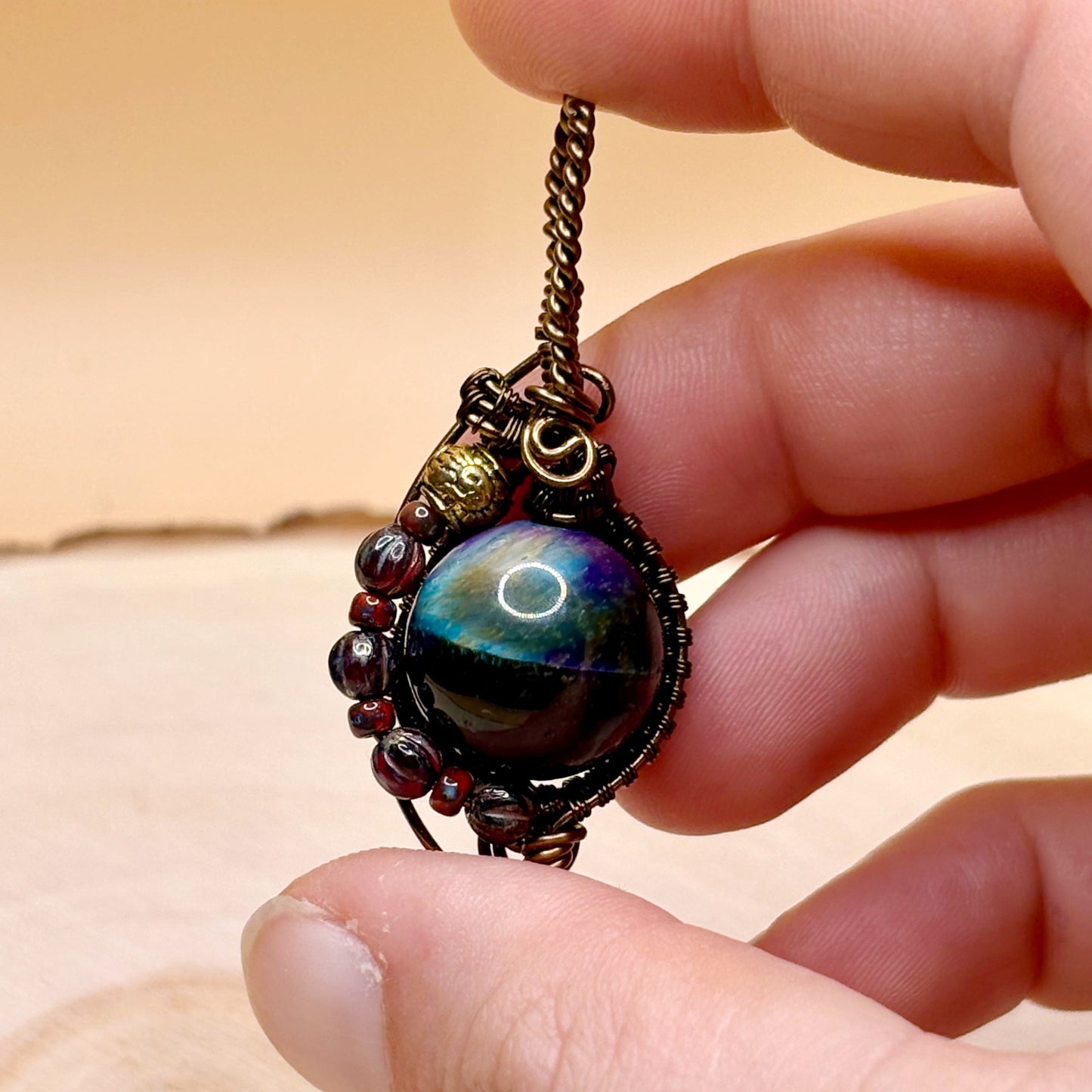 Hand holding a necklace with a multicolored gemstone pendant against a neutral background