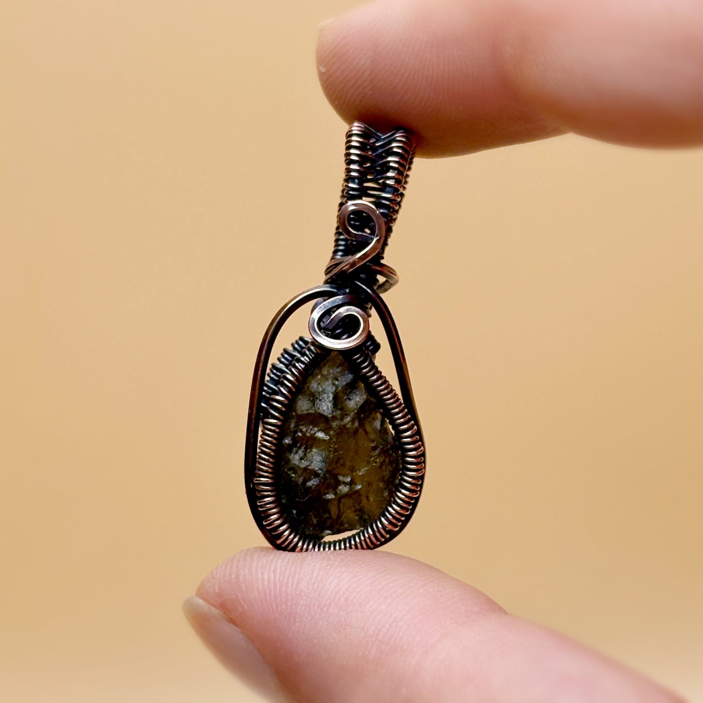 Hand holding a wire-wrapped pendant with a natural stone against a beige background