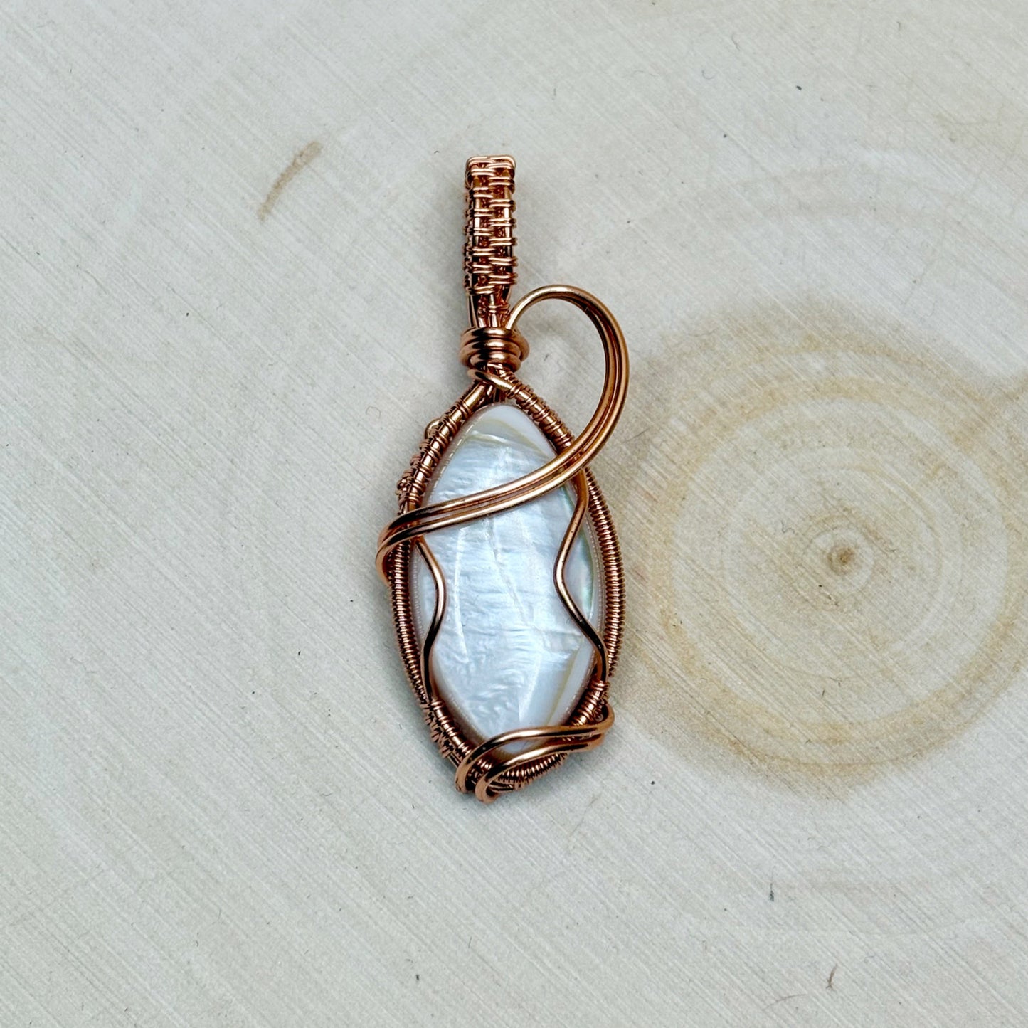 Mother of pearl shell with copper wire wrapping sitting on a light background