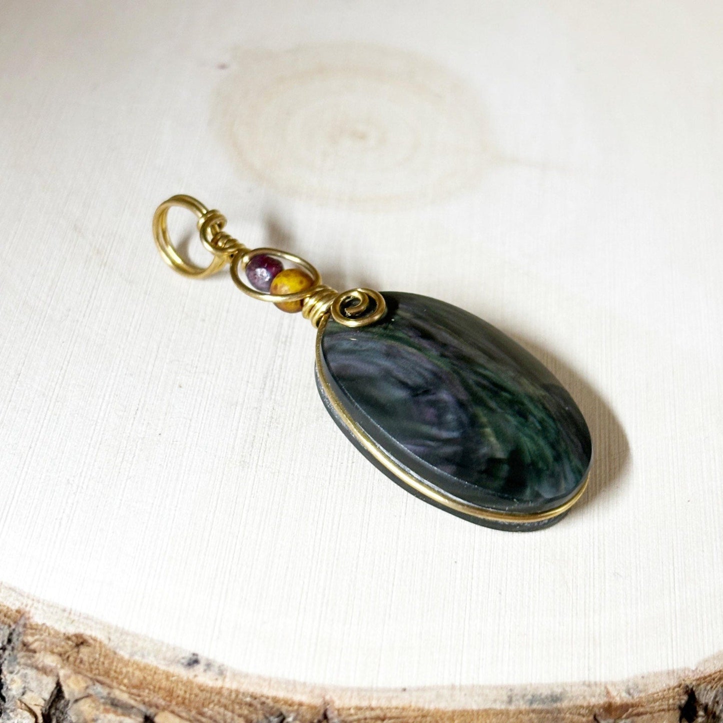 Wire Wrap Pendant in jewelers bronze with a rainbow black stone in the middle sitting on a white wooden background