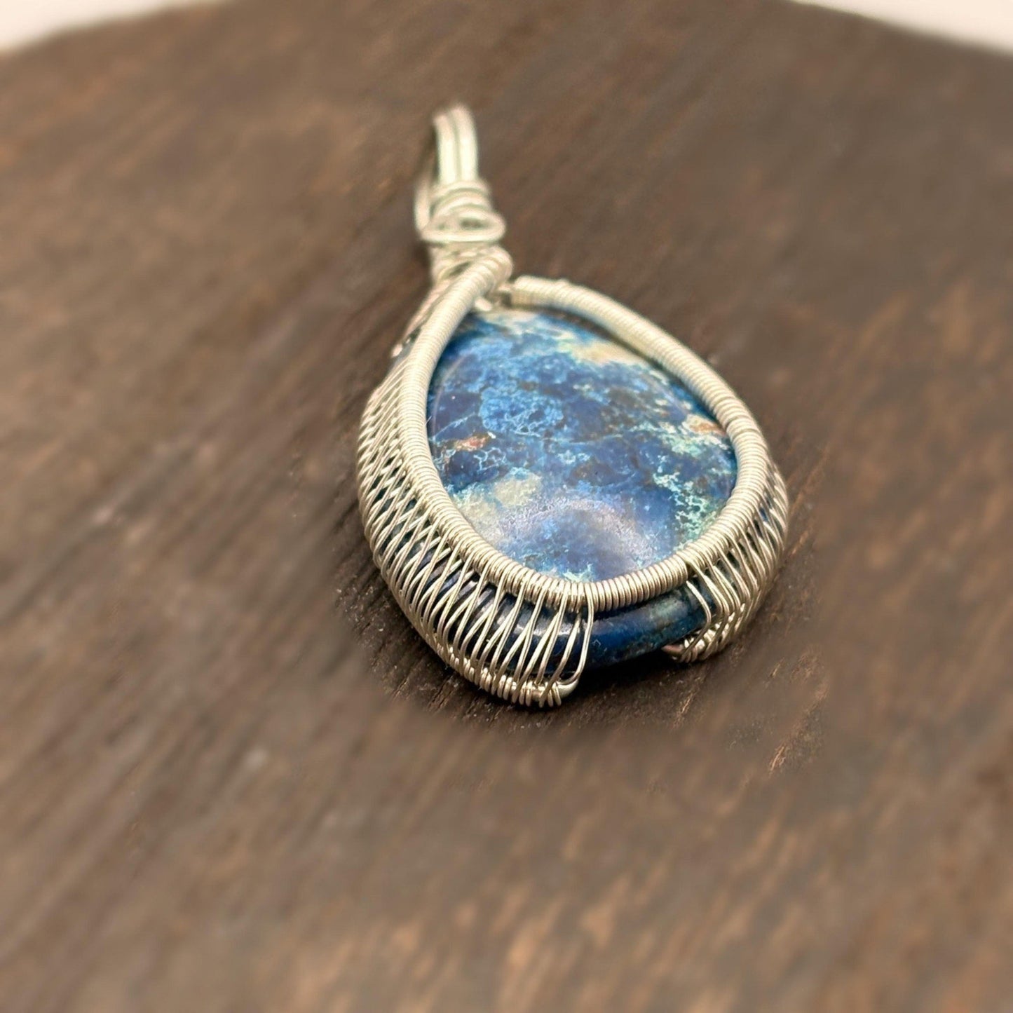 Blue stone pendant with silver wire wrapping on a wooden surface