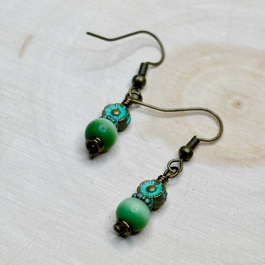 Pair of earrings with green beads and bronze hooks on a light wooden surface