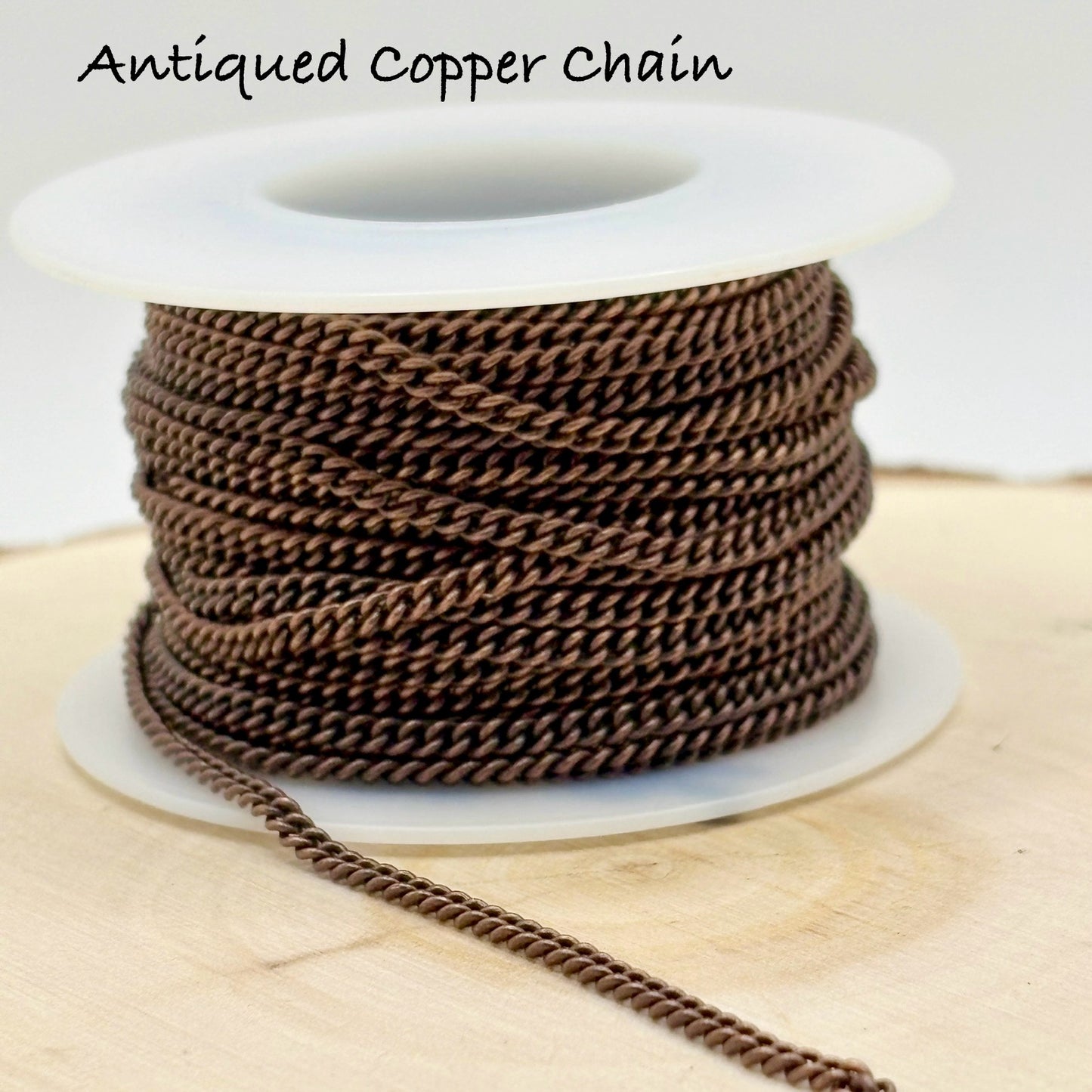 Spool of antique copper chain on a wooden surface with text 'Antiqued Copper Chain'.