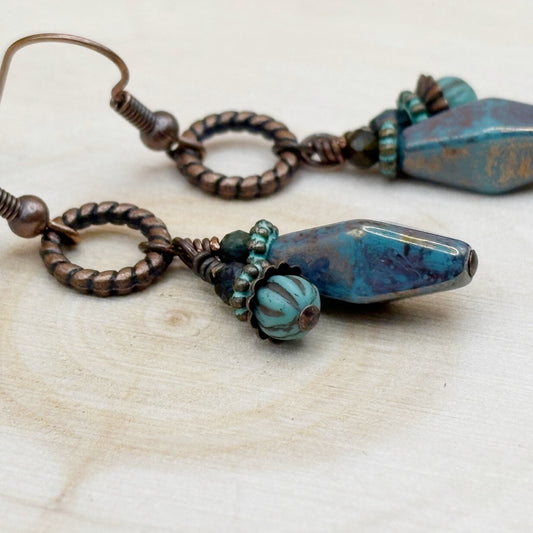 Pair of earrings with blue and brown beads on a light wooden surface