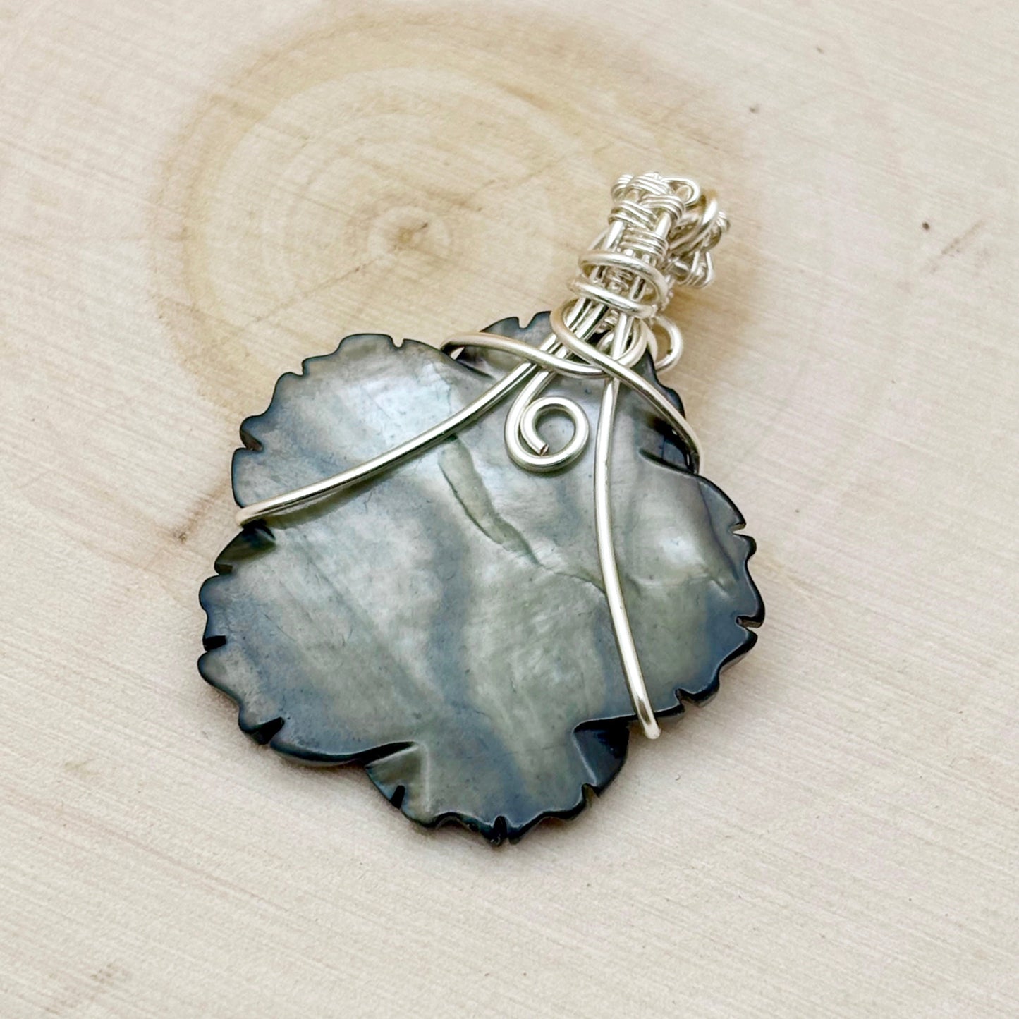 Pendant with shell-like design and silver wire wrapping on a wooden surface
