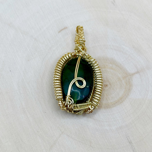Gold-wrapped pendant with a green stone on a light wooden surface