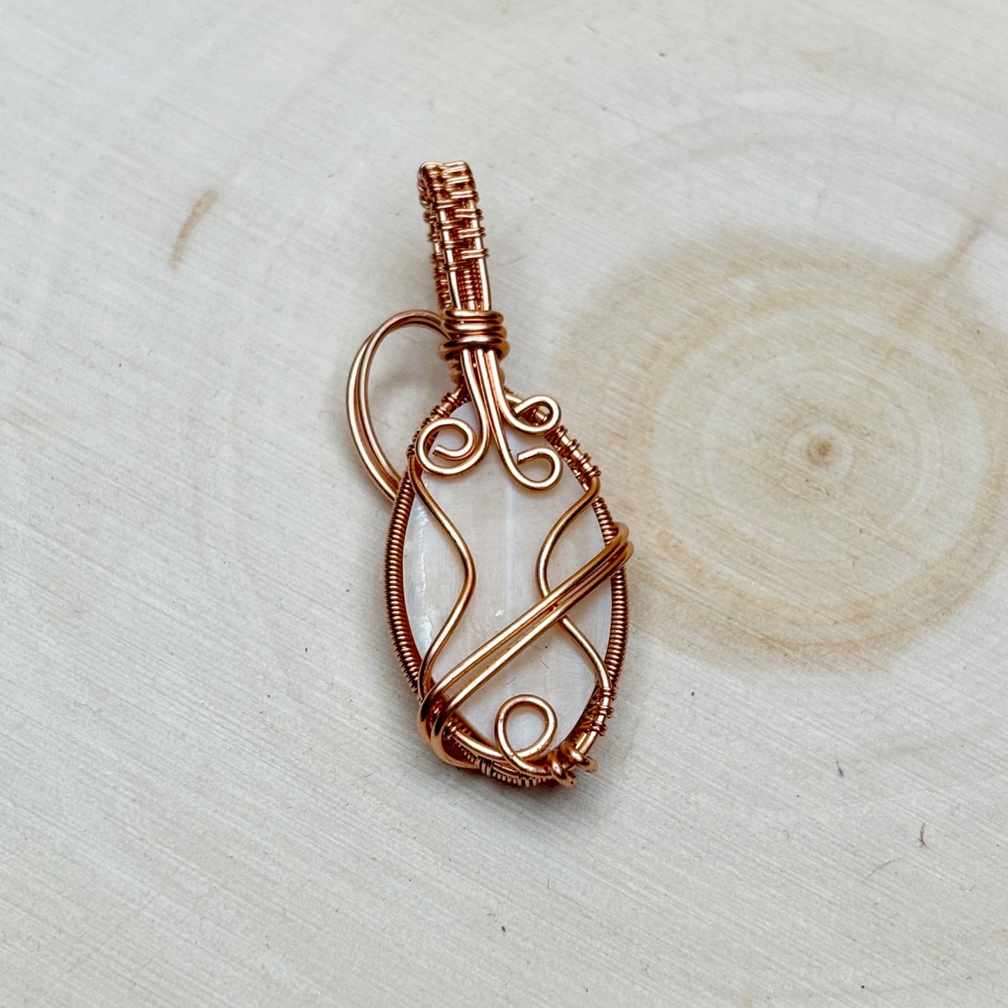 Copper wire-wrapped pendant on a light wooden background