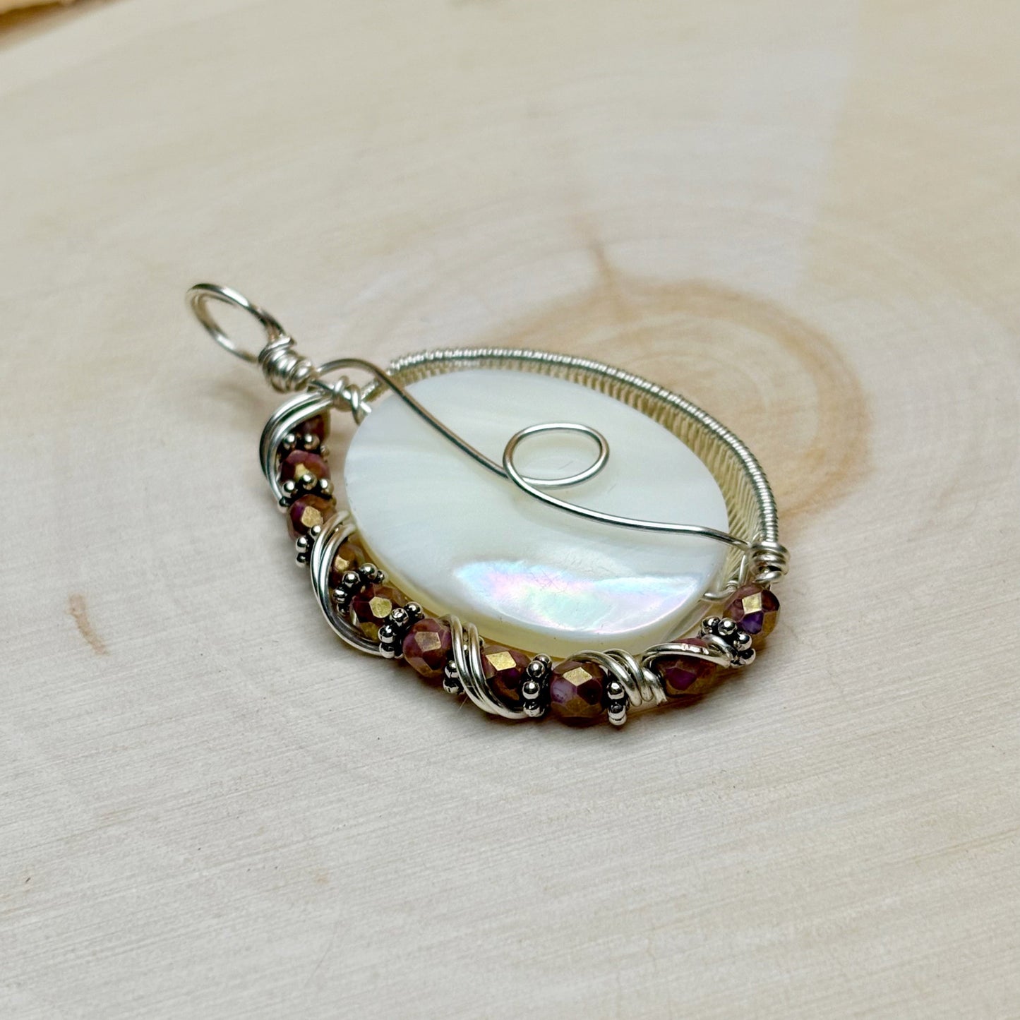 Jewelry pendant with a white shell and glass beads on a light wood background