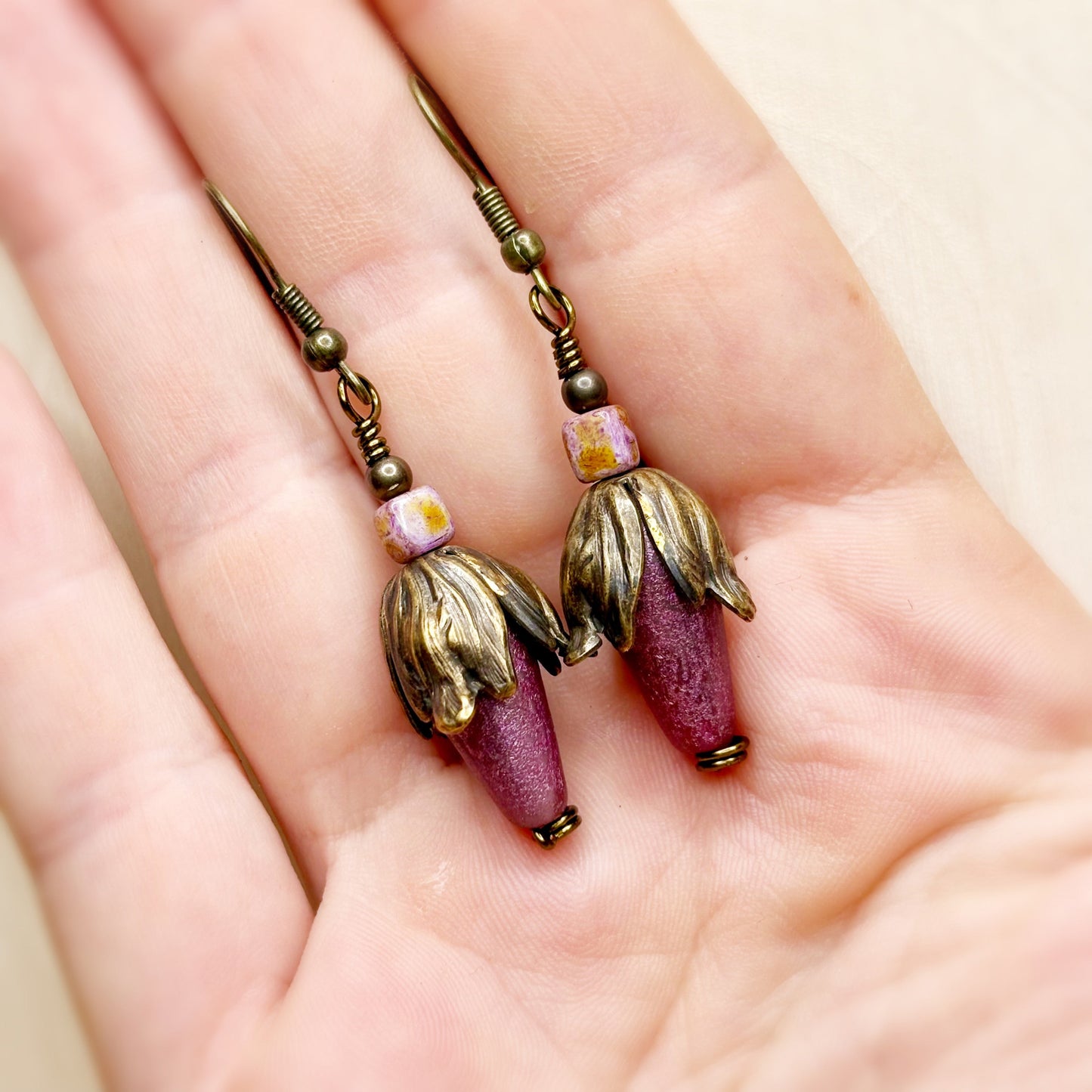 Pair of earrings with purple and gold components held in a hand.