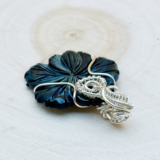 Blue pendant with silver wire wrapping on a textured white surface