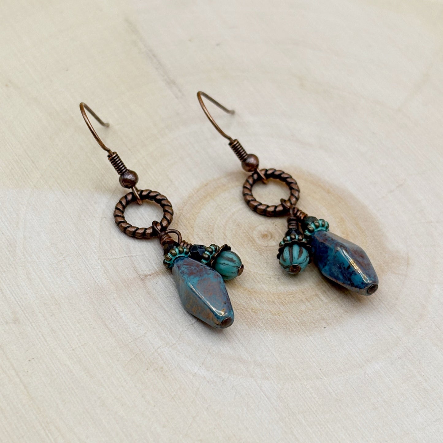 Pair of earrings with blue and copper elements on a light wooden surface