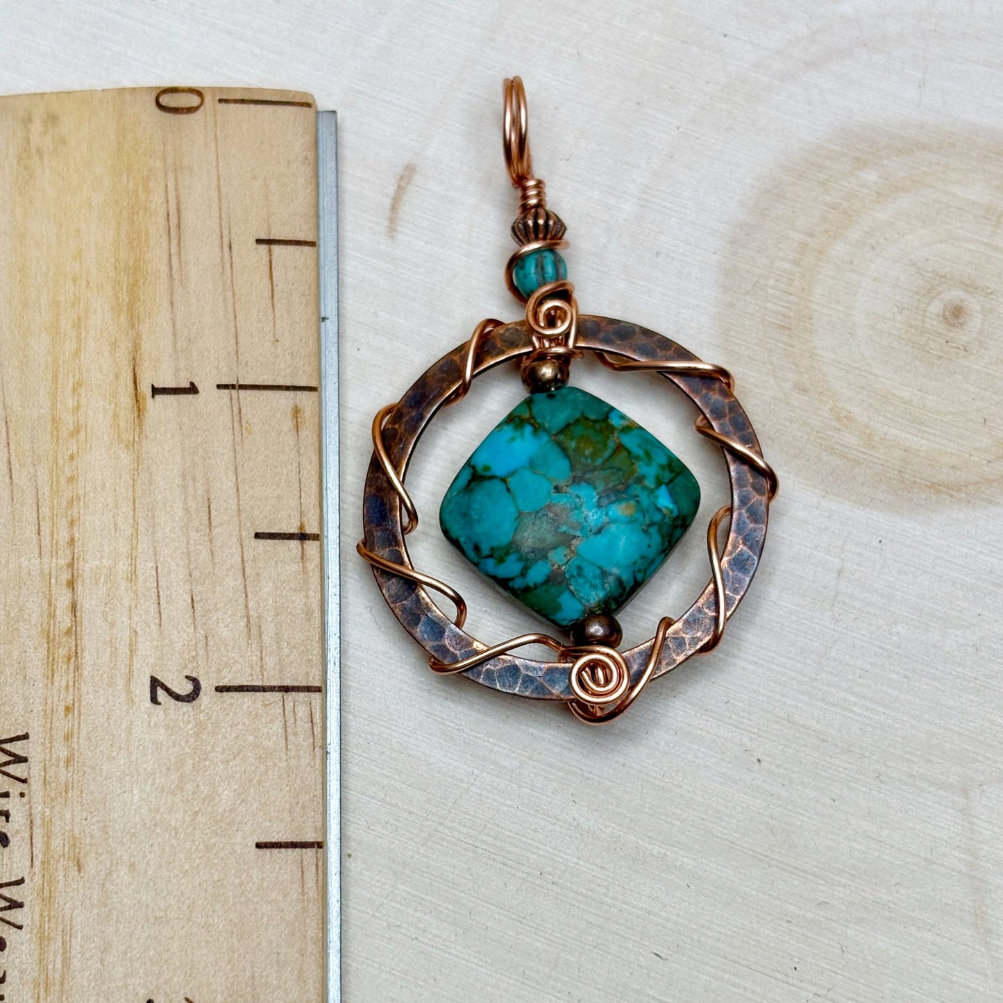Turquoise pendant with copper frame on a wooden surface with ruler for scale