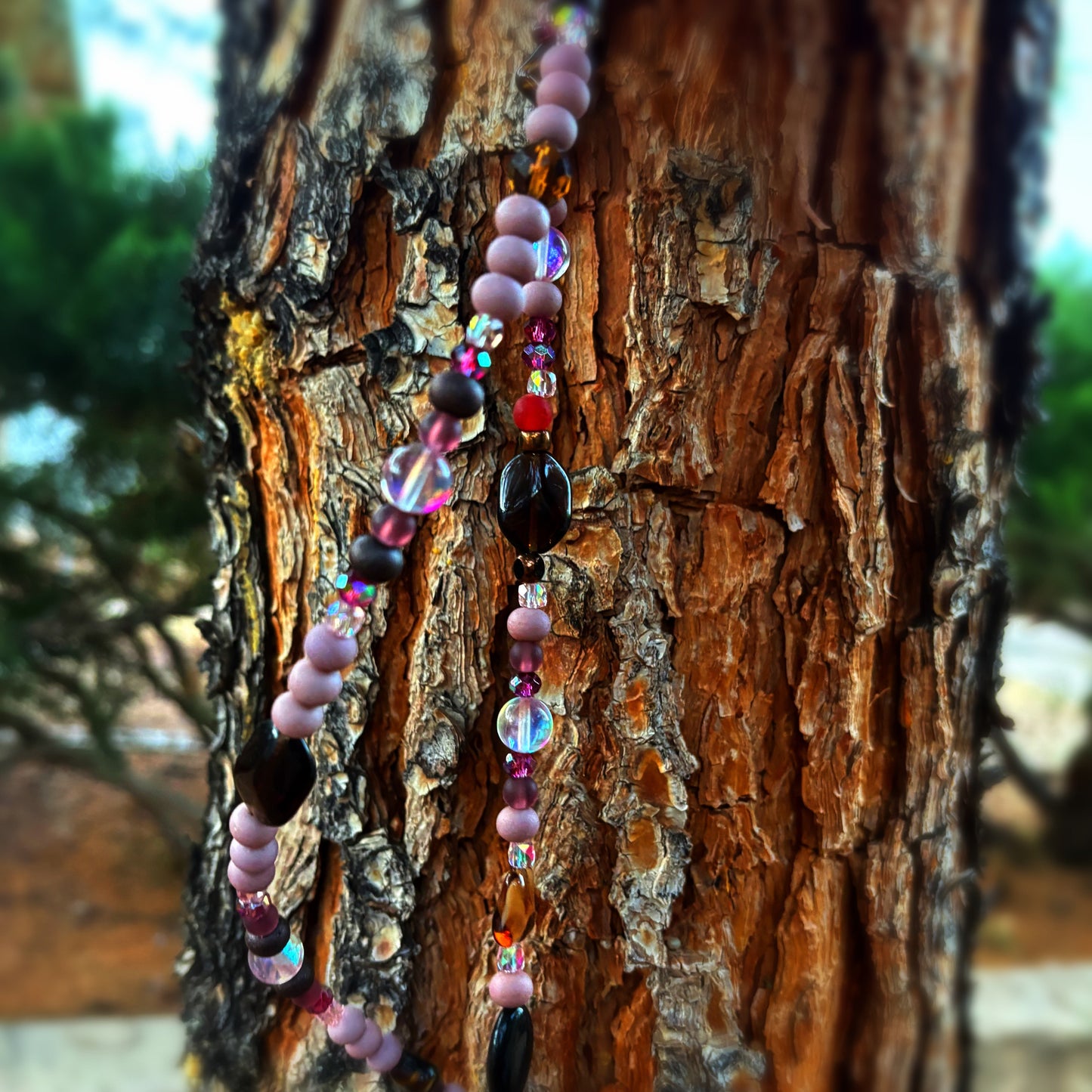 Beaded sun catcher with pink, black, and clear beads hanging on a tree trunk.