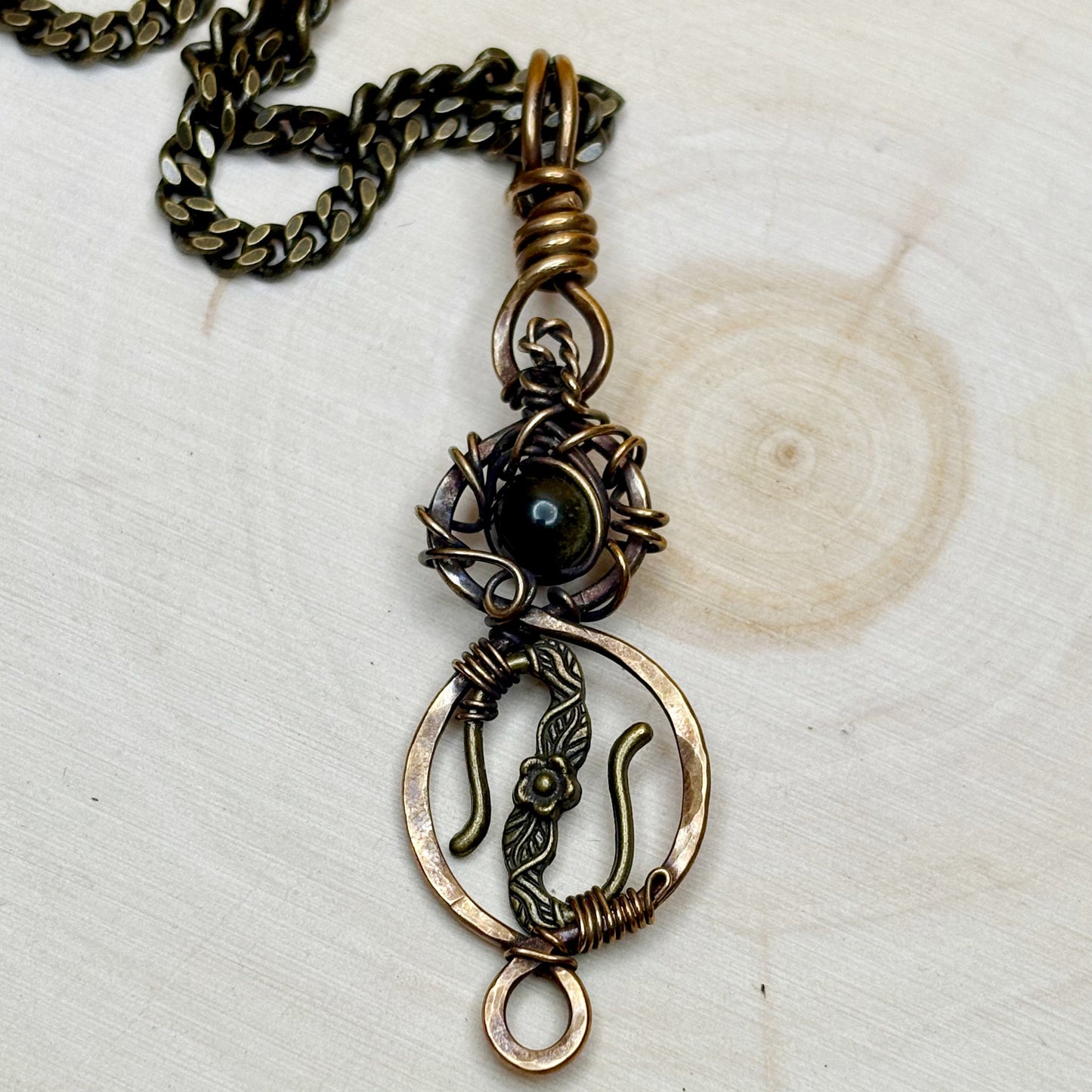 Bronze necklace with intricate pendant on a light wooden surface