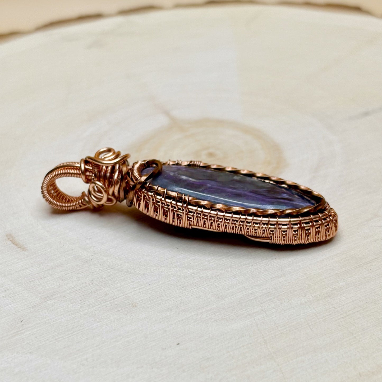 copper necklace pendant with purple stone on a textured beige surface
