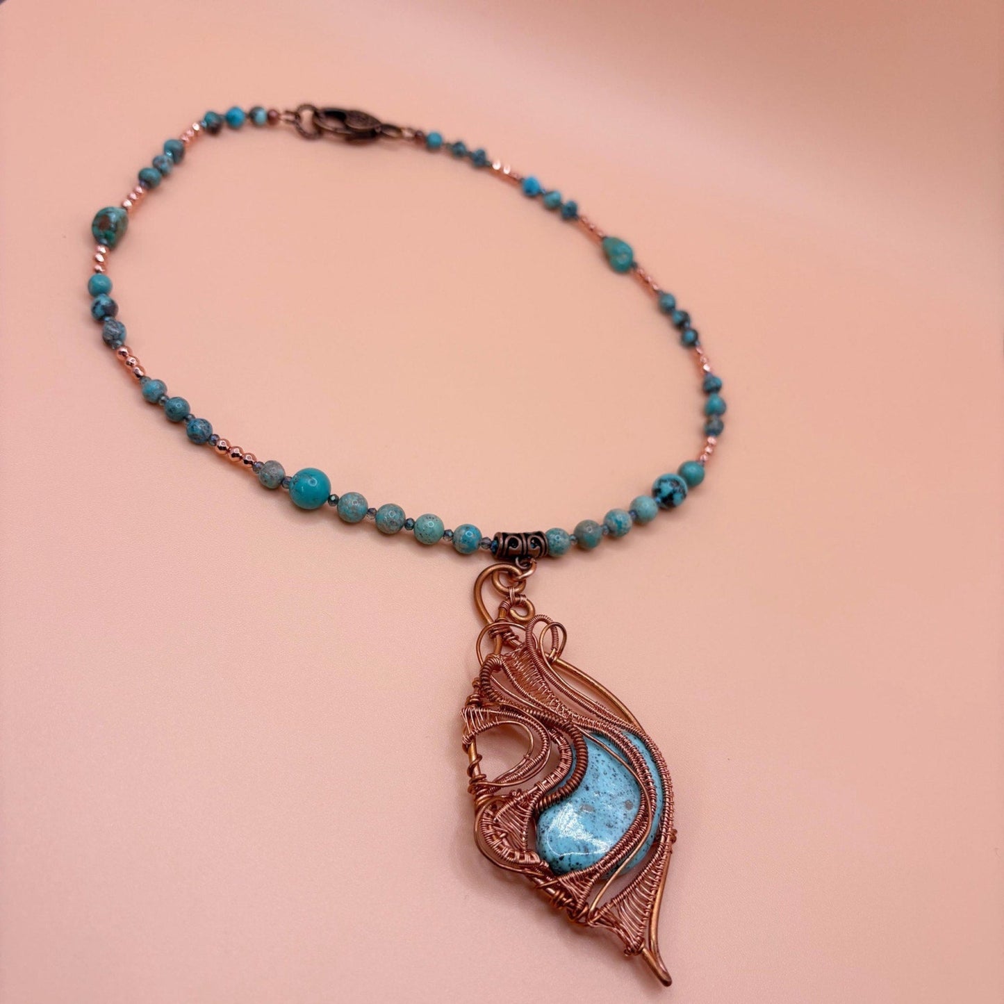 Necklace with a leaf-shaped pendant featuring turquoise stone on a peach background