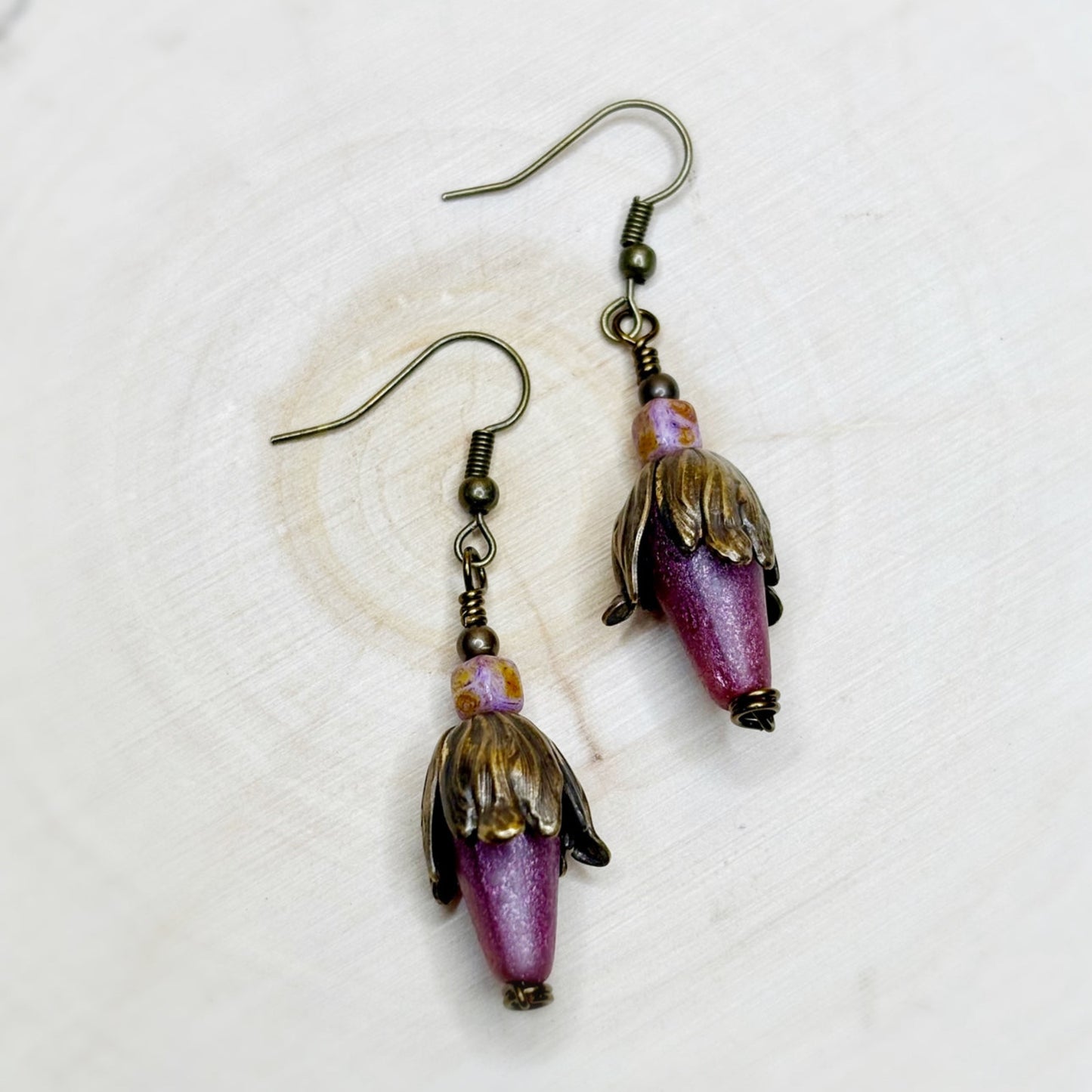 Pair of earrings with purple and gold beads on a white background