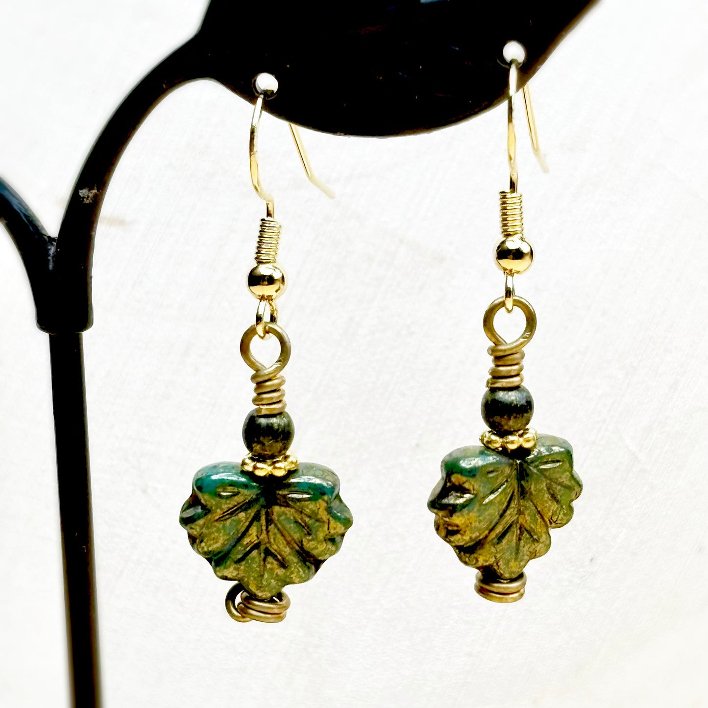Pair of green leaf-shaped earrings with gold accents on a white background