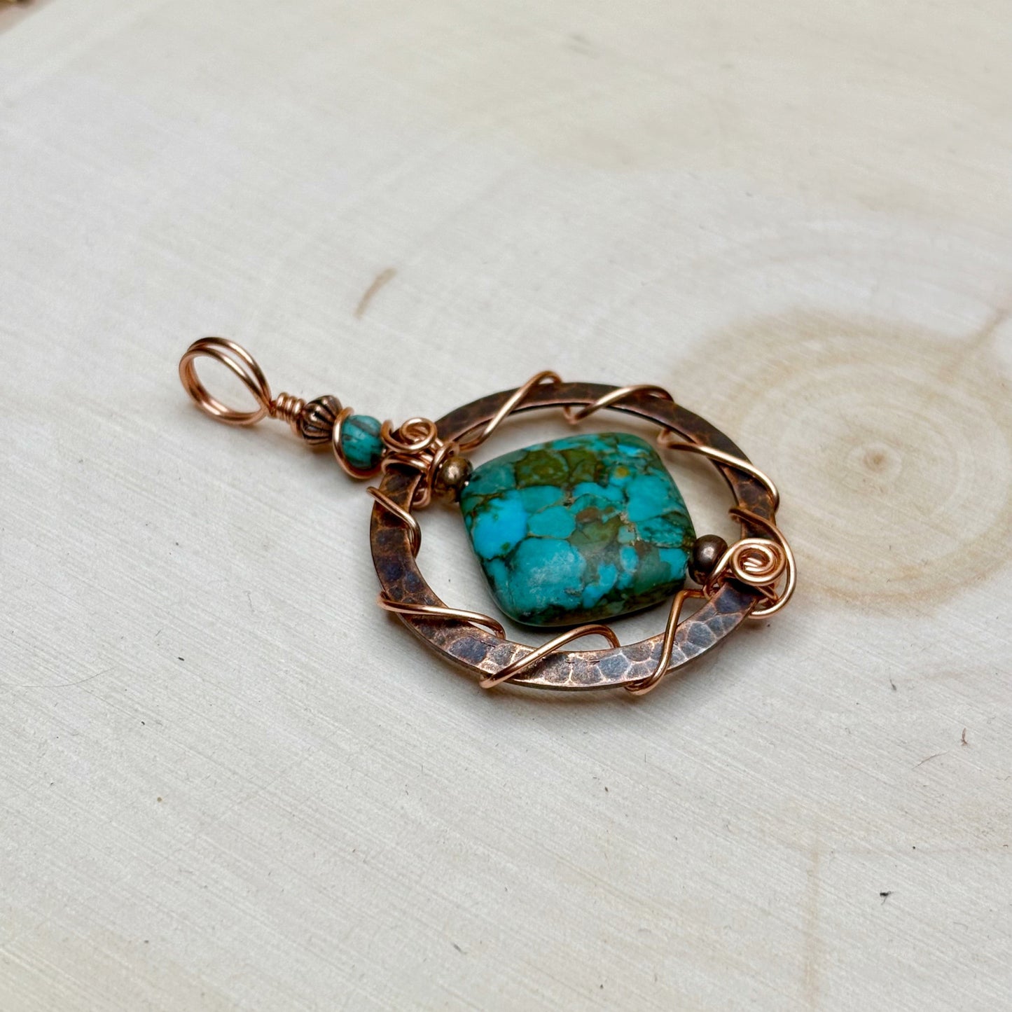 Turquoise stone pendant with copper wirework on a light wooden surface