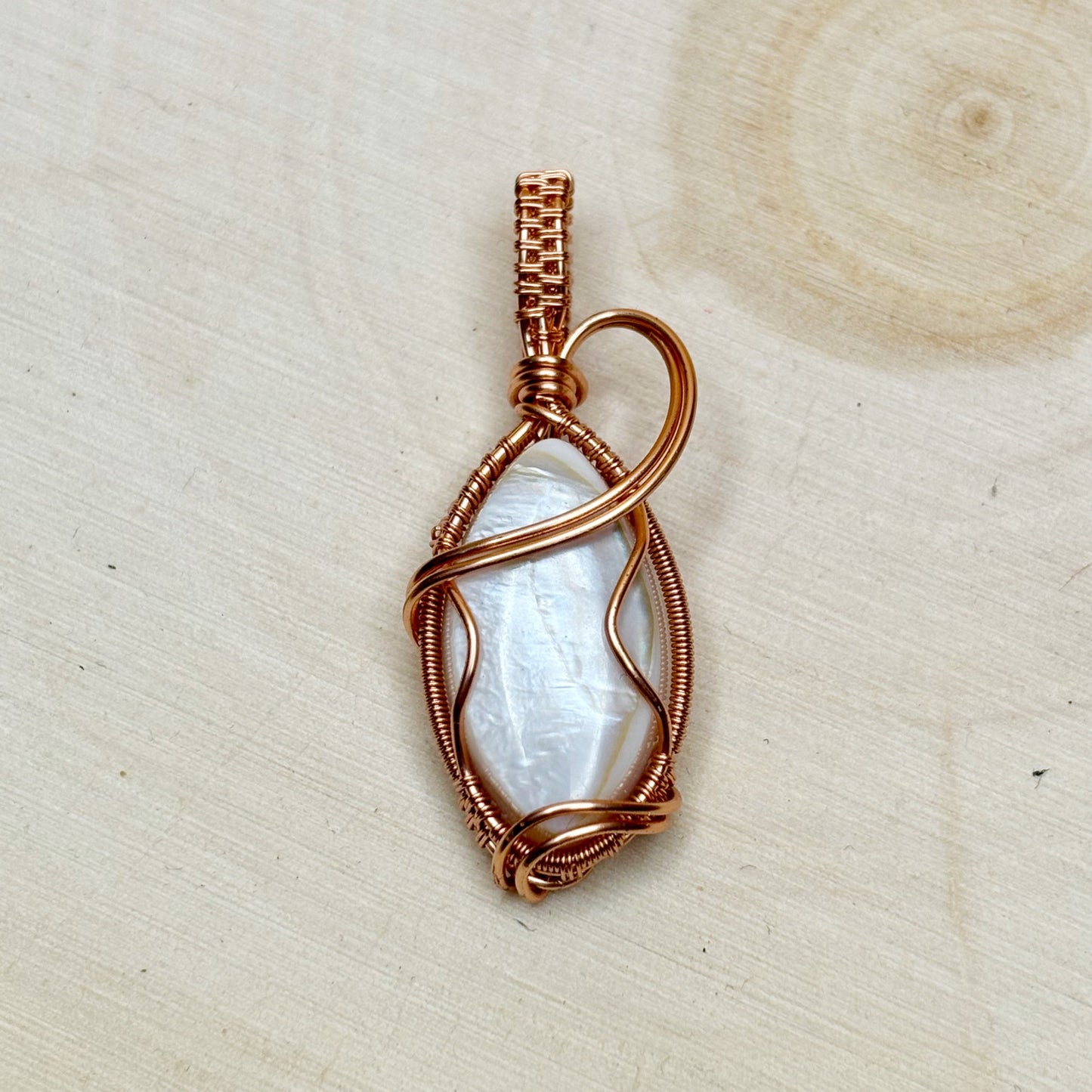 Copper-wrapped pendant with a white shell on a beige background