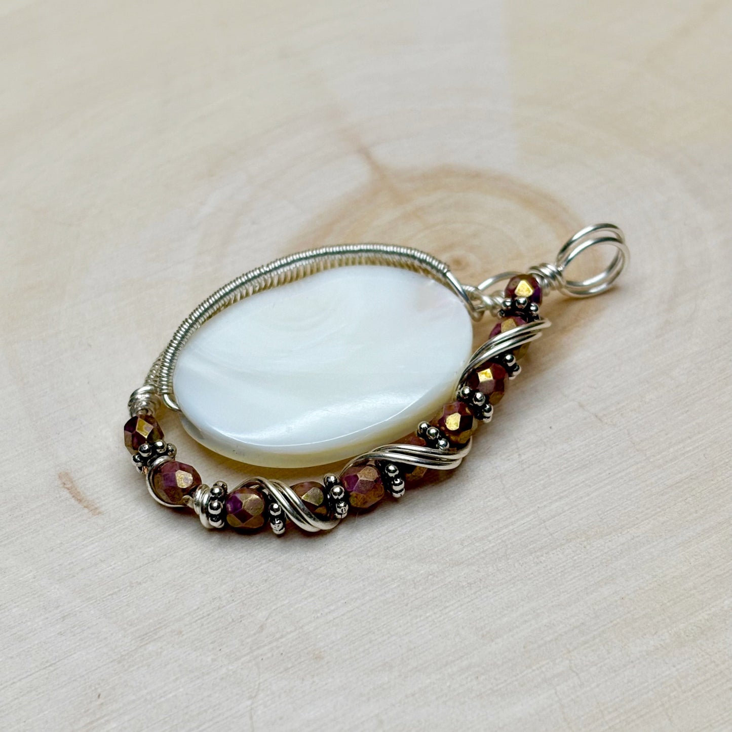 Mother of pearl shell wire wrapped in silver displayed on a wooden background