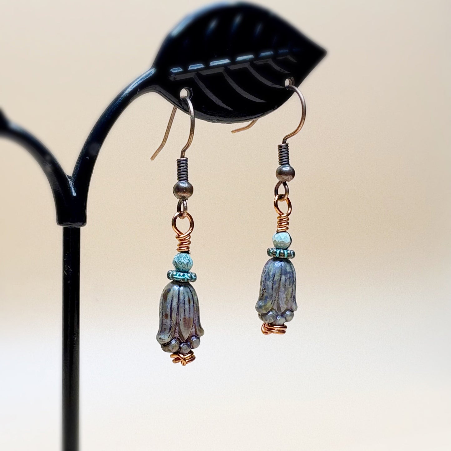 Pair of earrings with blue and bronze beads on a black stand against a beige background