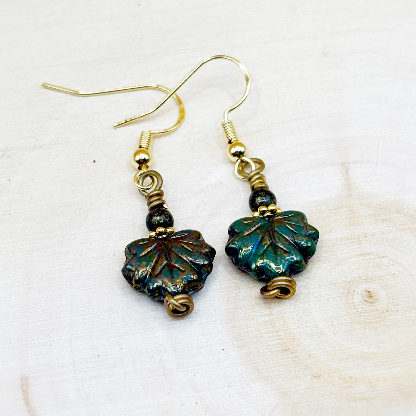 Pair of earrings with leaf-shaped beads on a light wooden surface